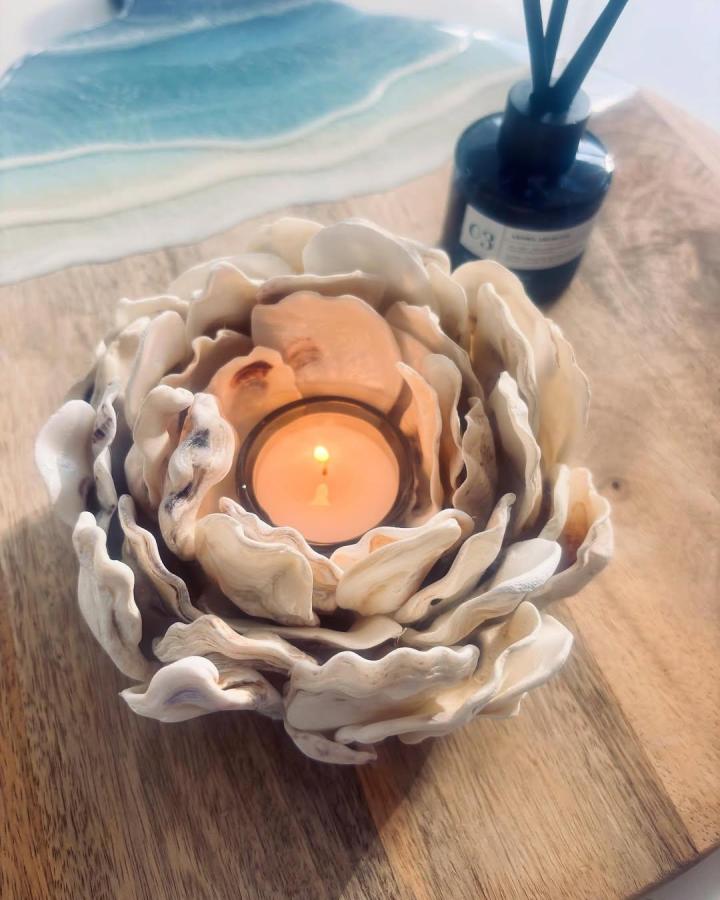 Ivory shell candle holder from @waterside_treasures. Layered shells surround a glowing peach candle.
