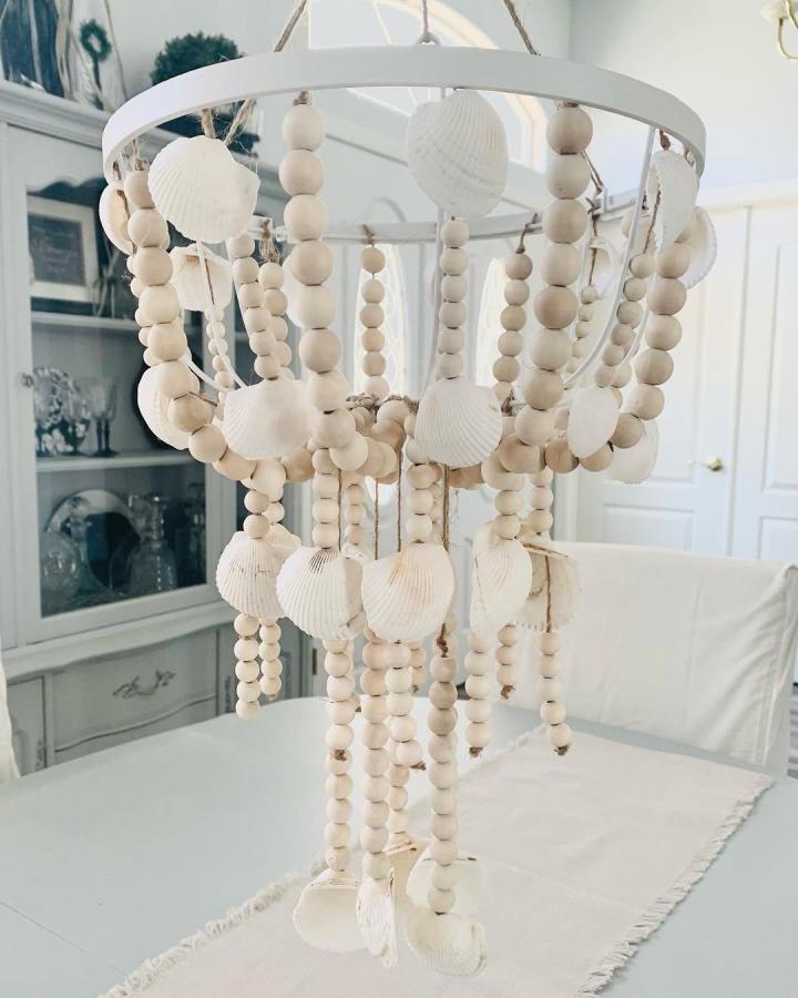 Ivory seashell and natural wood bead hanging craft from @whitesparrowliving. Coastal chandelier with layered strands.