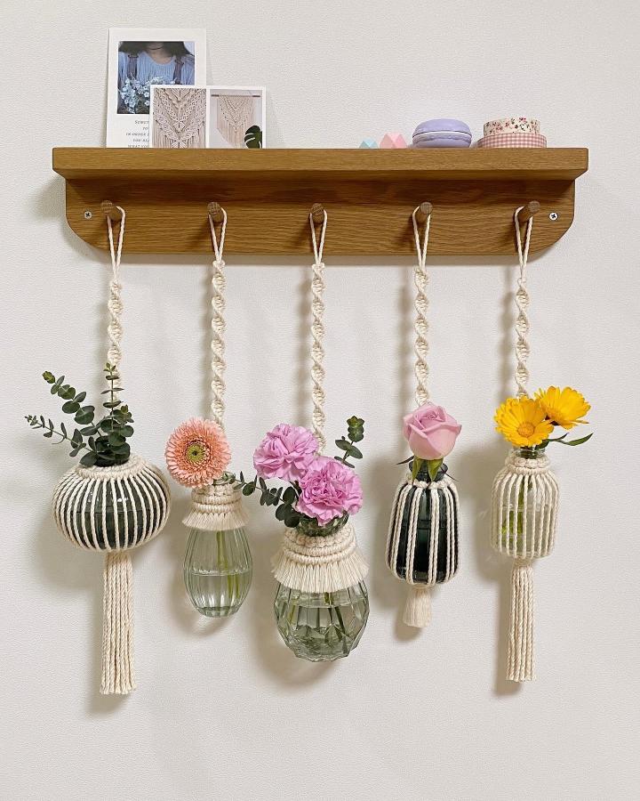 Cream macramé flower holders from @letme_bemyself. Knotted cords suspend striped vases and fresh pink, yellow, and orange blooms.