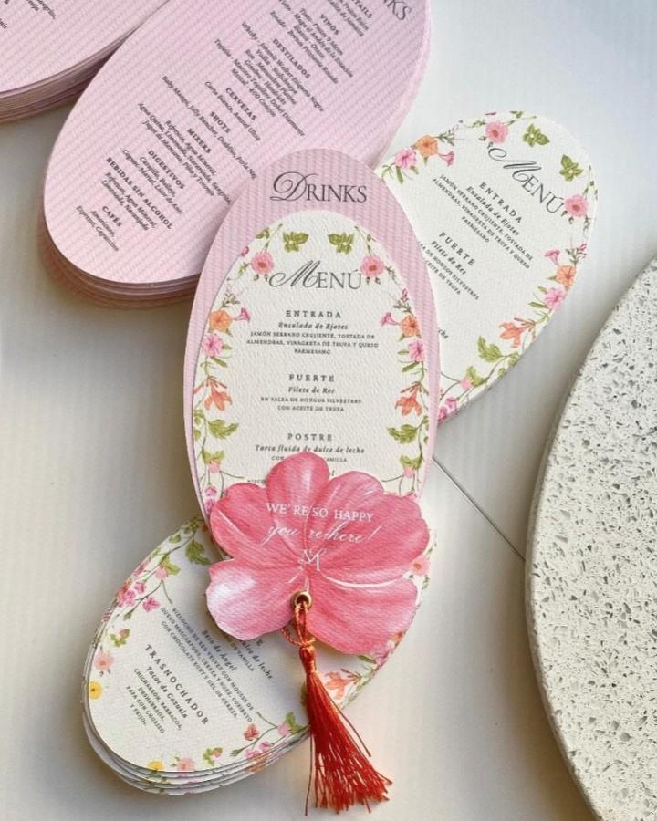 Floral pink oval menu card from @papellio.co. A handmade wedding paper craft with a flower embellishment and red tassel.