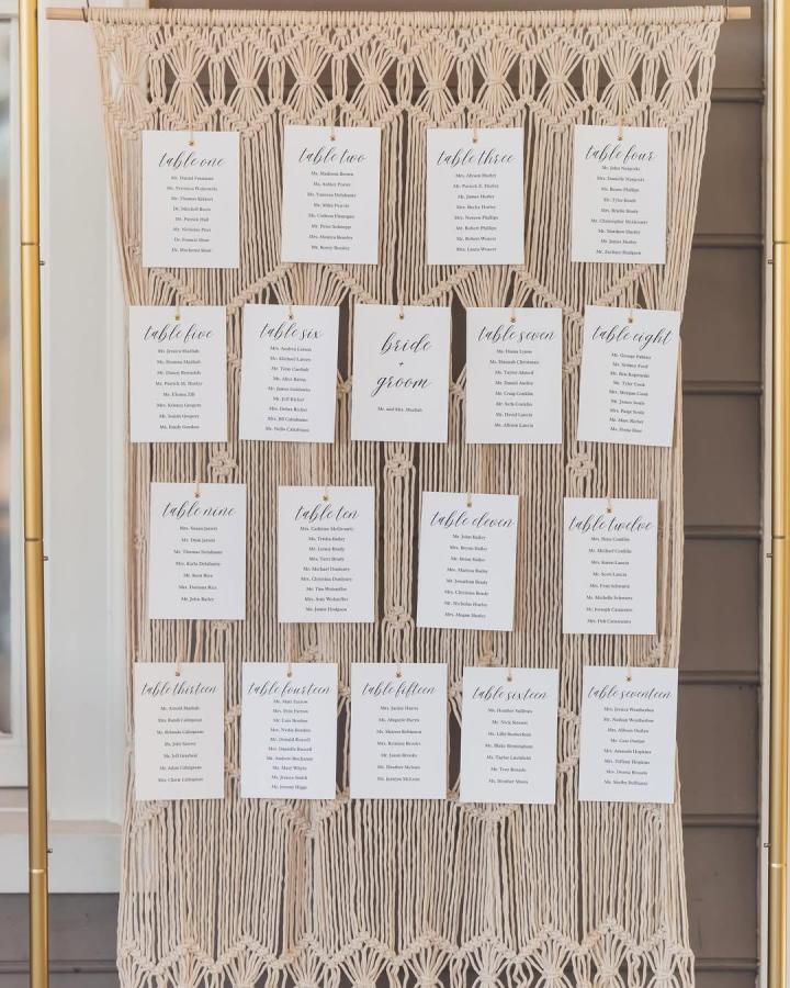Cream macramé seating chart from @rosiethewanderer. Ivory table cards hang from a textured handmade wedding display.