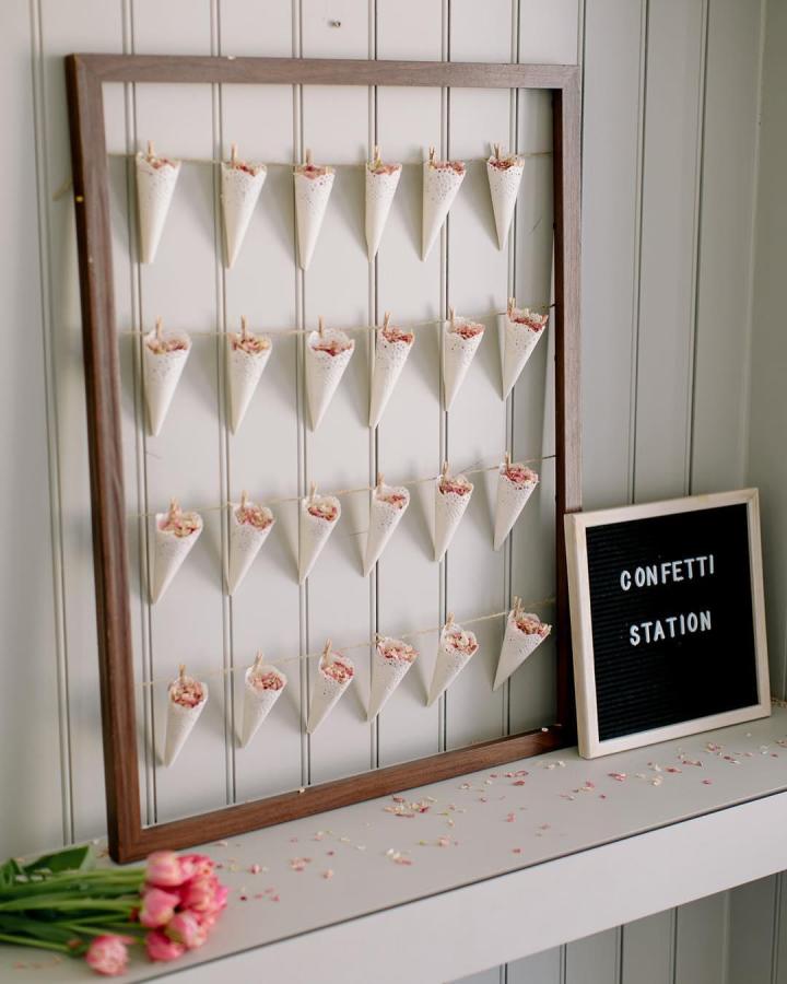 Ivory paper confetti wall from @rockmywedding. Rosy petals fill hanging cones for a charming wedding craft display.
