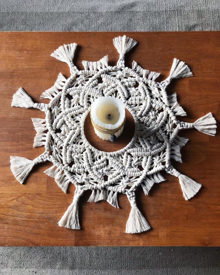 Cream macramé candle mat from @ak_macrame. Tassels frame a handmade wedding tabletop accent.