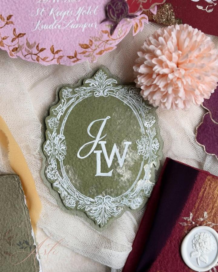 Olive green ornate monogram plaque from @madebyarti. Blush flower, burgundy textiles, and gauze style a handmade wedding detail.
