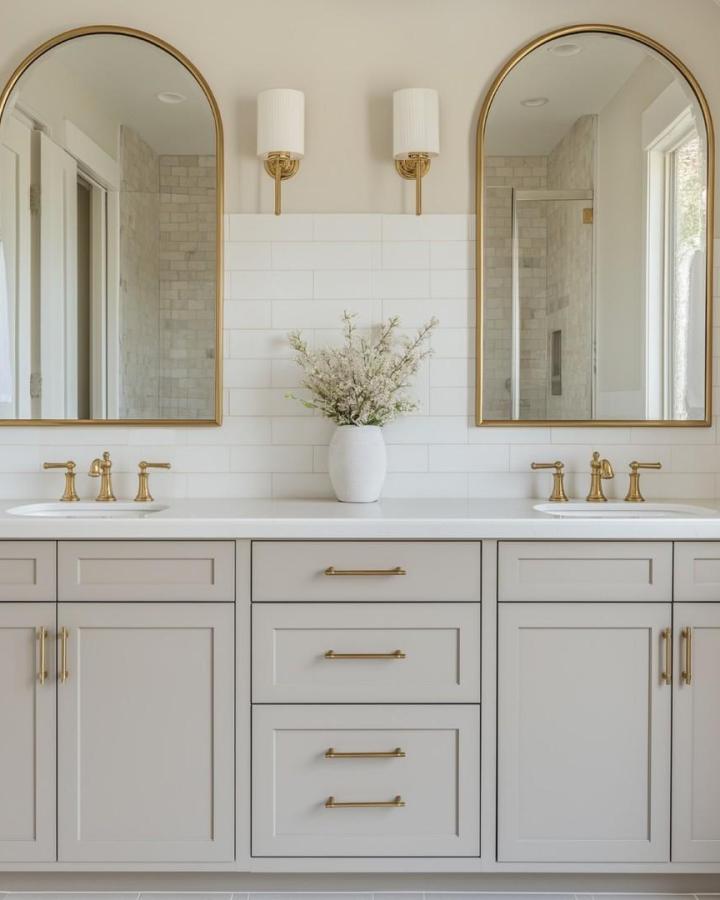 Warm white double vanity from @acshomeshow. Arched gold mirrors and matching faucets brighten the bathroom.