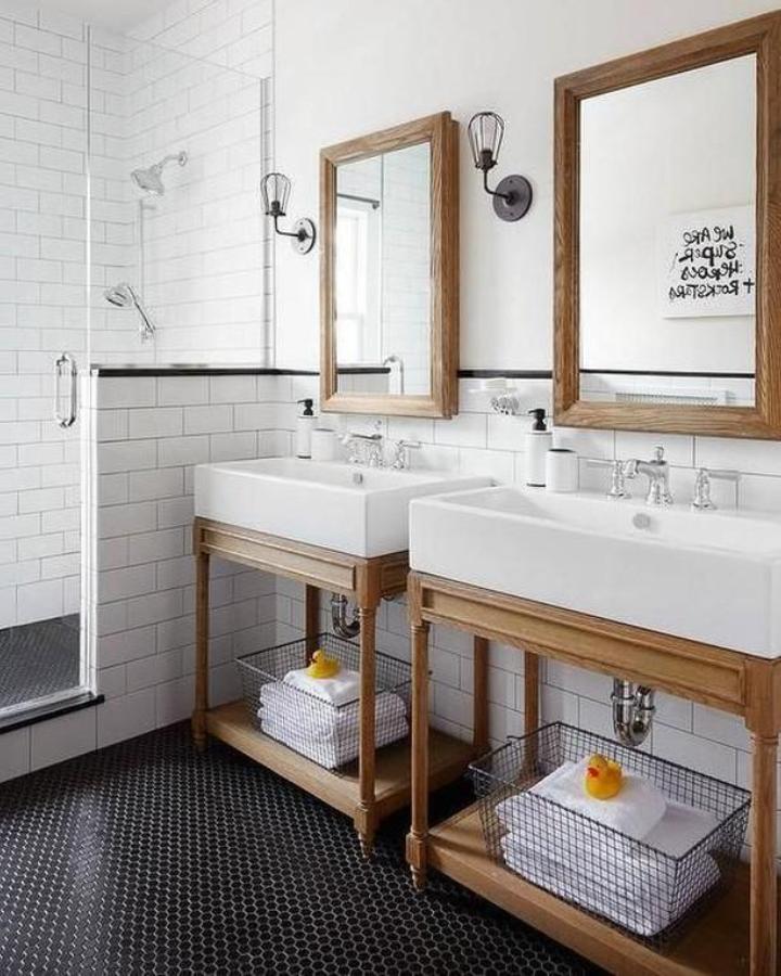Warm wood double vanity from @lscostless. White subway tile, black penny tile floor, and twin pedestal sinks.