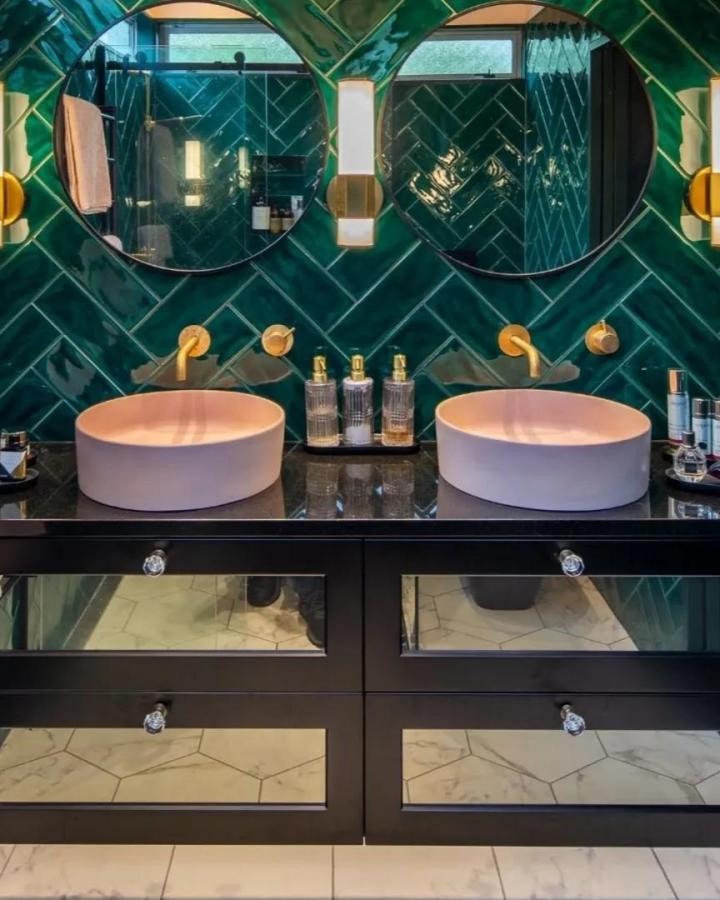 Emerald double vanity bathroom from @design_goddess. Round mirrors, pink vessel sinks, brass faucets, and black cabinetry create jewel-toned contrast.