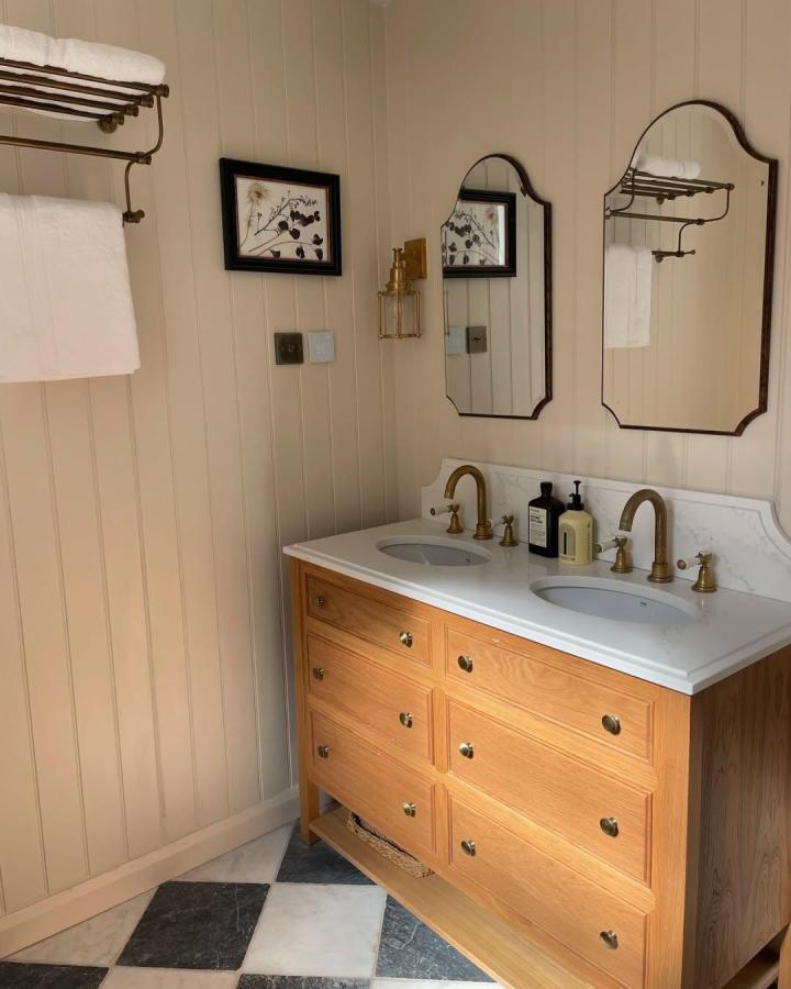 White oak double vanity from @four__home. Vintage brass fixtures, arched mirrors, and two oval basins.