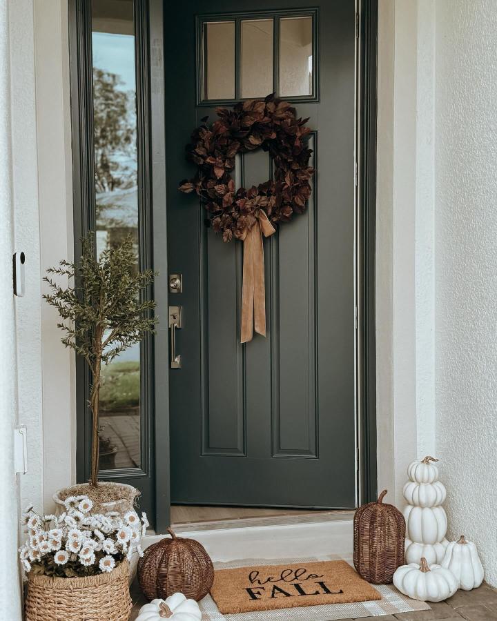 Dark leafy wreath and white pumpkins from @whereheartresides. Cozy fall front door decor ideas with wicker accents.