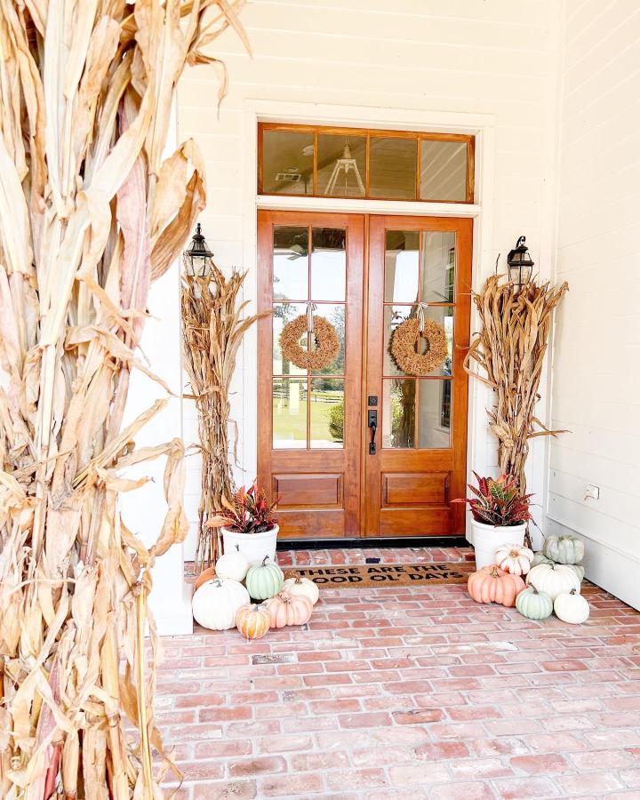 Warm natural corn-stalk front entry from @oldoaksfarmhouse. Wreaths, pumpkins, and white siding create welcoming autumn curb appeal.