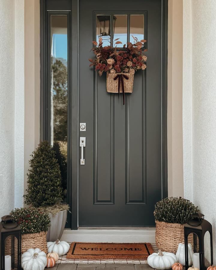 Rust-toned woven basket front door from @whereheartresides. Harvest florals and white pumpkins create a welcoming autumn entry.