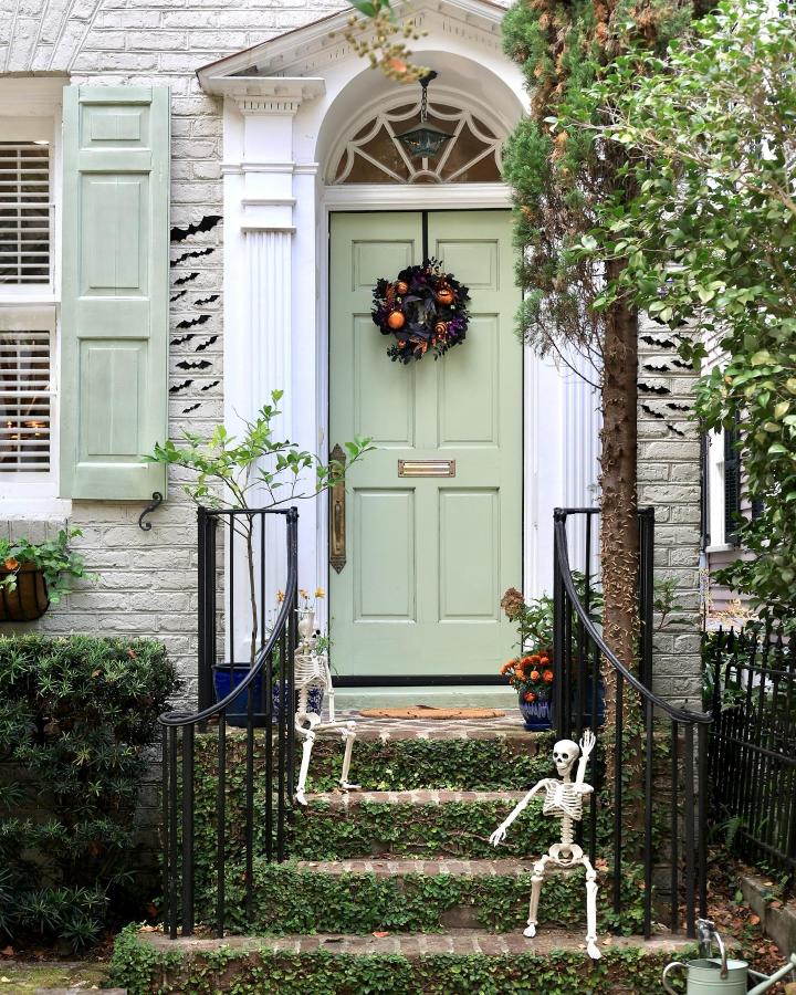Sage green Halloween front door from @thecharlestonlens. Wreath, skeletons, ivy steps, and fall front door decor ideas.