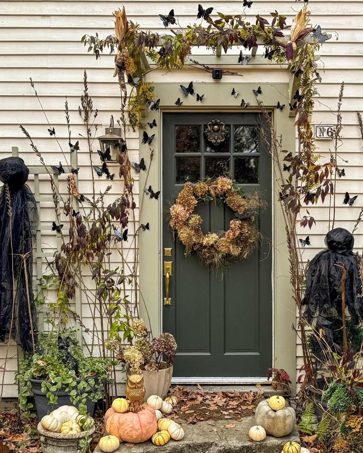 Dark green butterfly wreath entryway from @mstarrevdesign. Layered pumpkins and dried plants frame fall front door decor ideas.