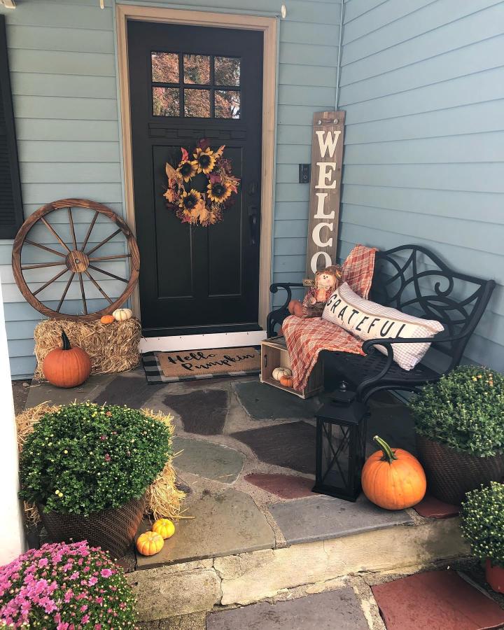 Rustic pumpkin porch from @thepartyplanningnurse. Fall front steps decor ideas feature mums, hay bales, sunflower wreath, and grateful bench.