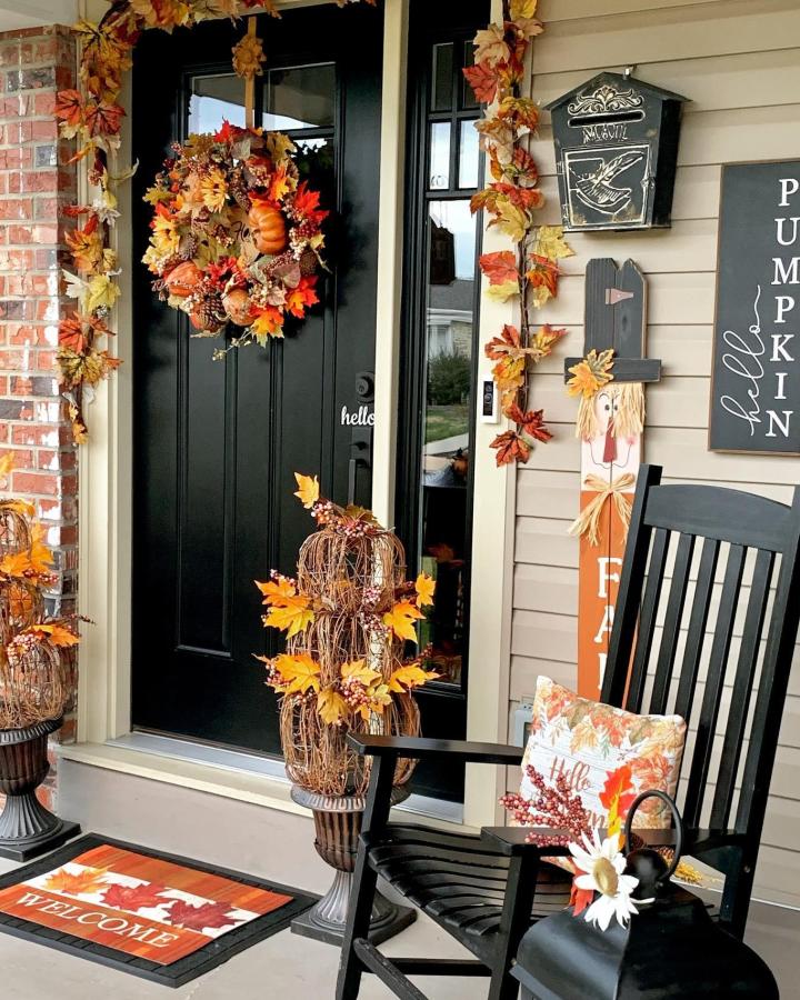 Black and orange fall front steps decor ideas from @decor_ate_with_sharon. Leaf garlands frame a wreath and rocking chair.
