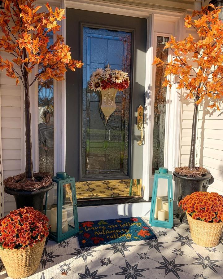 Orange faux-leaf branches and orange mums frame a fall front entry from @simplestarfishhome. Teal lanterns brighten the porch.