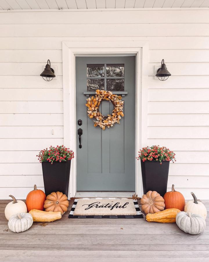 Amber wreath and gray front door from @nofolife. Pumpkins, planters, and grateful doormat create a welcoming autumn entryway.