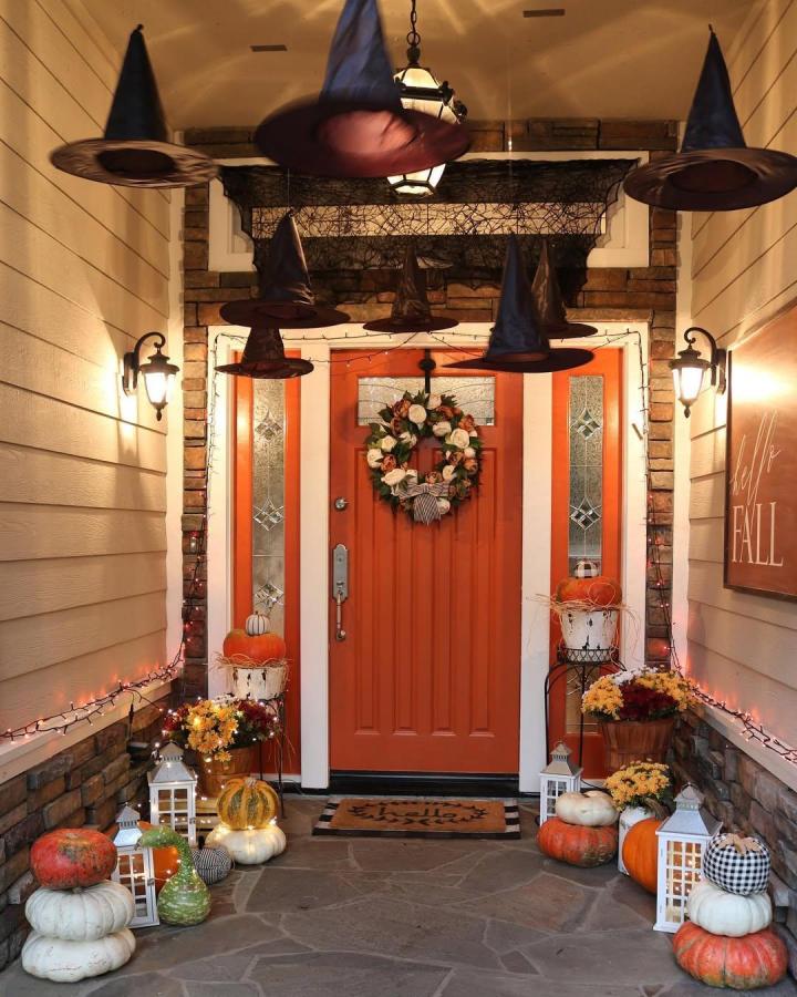 Black and orange hanging witch hats from @jodie.thedesigntwins. Pumpkin-lined porch with lanterns and autumn mums.