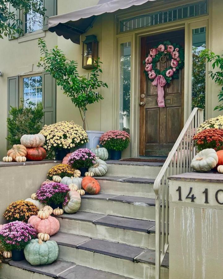 Pink floral wreath and potted mums from @elizabethalpaughart_design. Layered pumpkins brighten welcoming autumn steps.