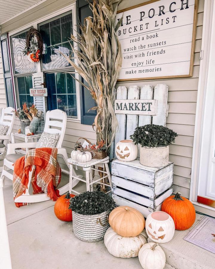 Cream And Orange Farmhouse Front Steps From @littlelovenest. Cornstalks, pumpkins, crates, and rocking chairs create a cozy autumn entry.