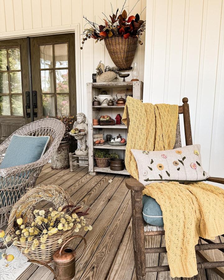 Rust and mustard woven porch display from @rachel_thepondsfarmhouse. Wicker basket, floral pillow, and cozy throws welcome autumn.