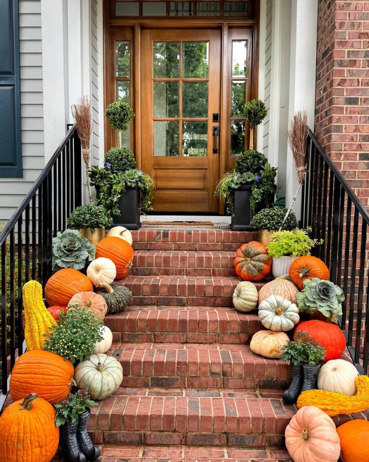 Orange and cream pumpkin staircase from @grandentrydoors. Layered fall entry with greenery and cornstalks.