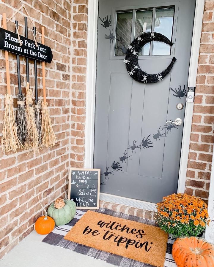 Black Halloween front door from @taylorhouseof3. fall front steps decor ideas feature spiders, pumpkins, mums, and a witchy doormat.