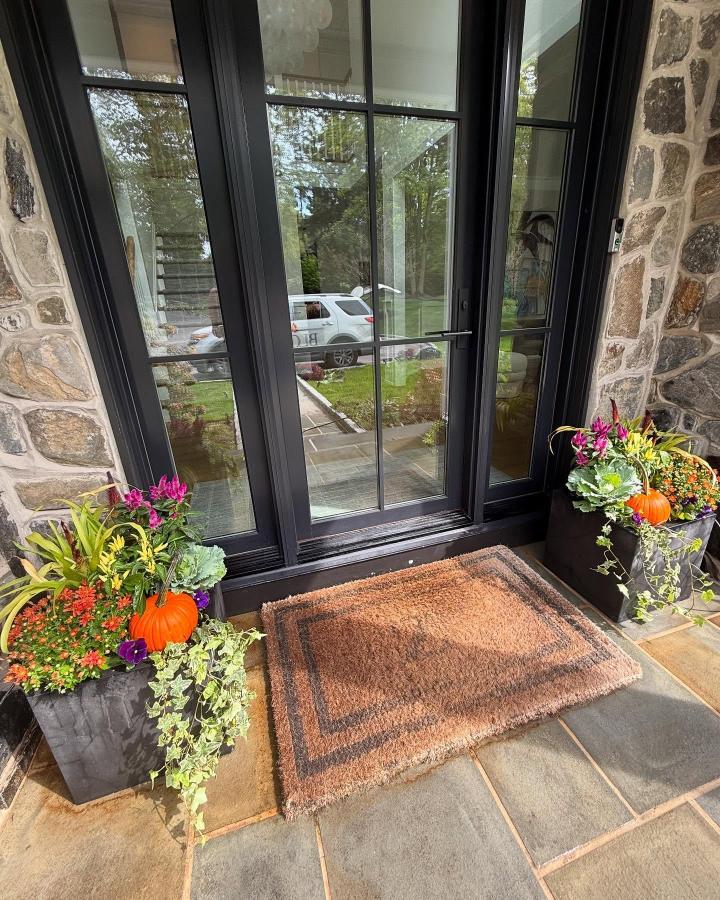 Black stone porch planters from @bloomdesign_andcontainers. Colorful fall planter ideas with pumpkins, flowers, cabbage, and trailing ivy.
