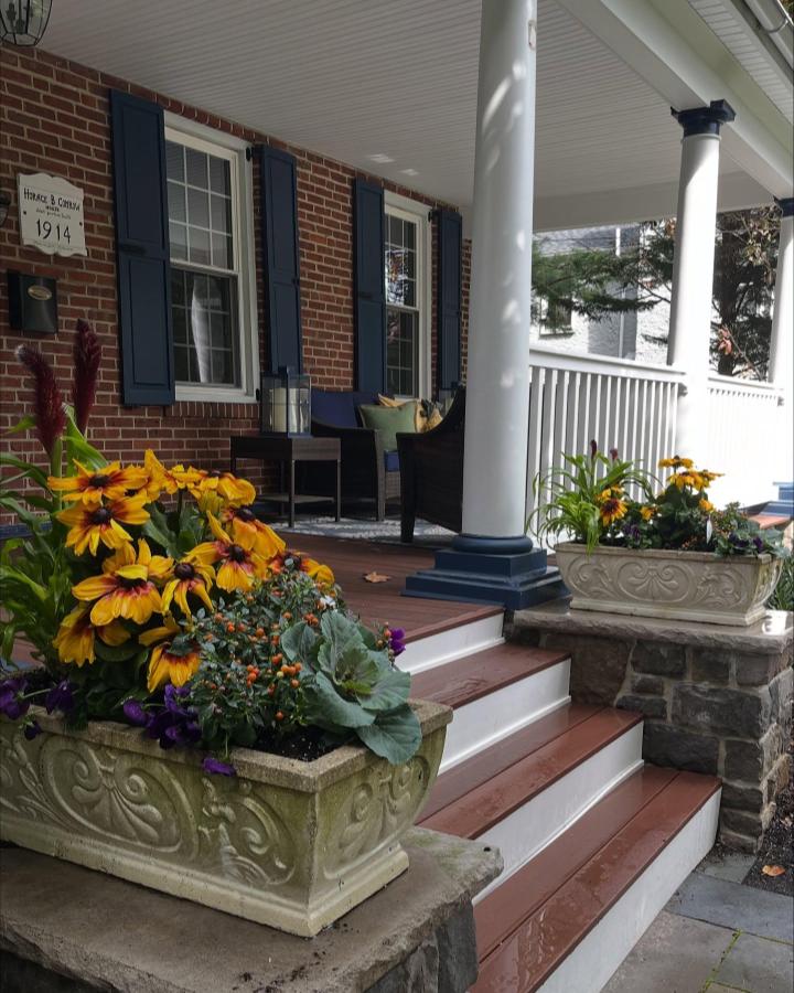 Ornate stone porch planters from @primopotsandplanters. Golden flowers, purple pansies, and silvery cabbage frame brick steps.