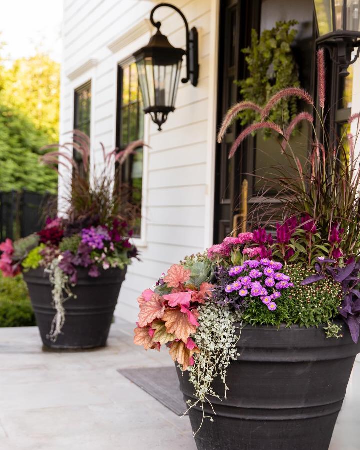 Black and jewel-toned porch planters from @jessicareissphotography. Pink plumes and purple blooms flank a white entryway.