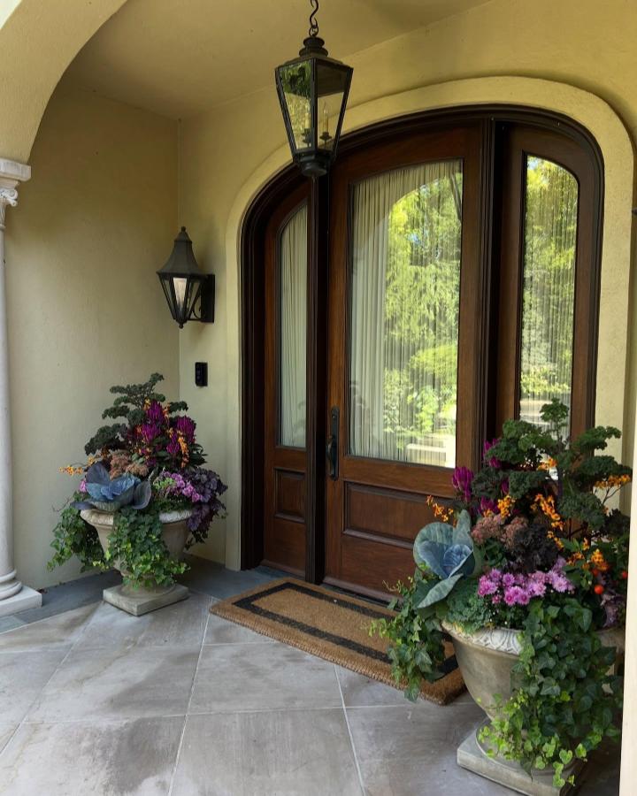 Stone and jewel-toned entryway planters from @thecontainedgarden. Lush ivy, purple mums, ornamental kale, and orange flowers.