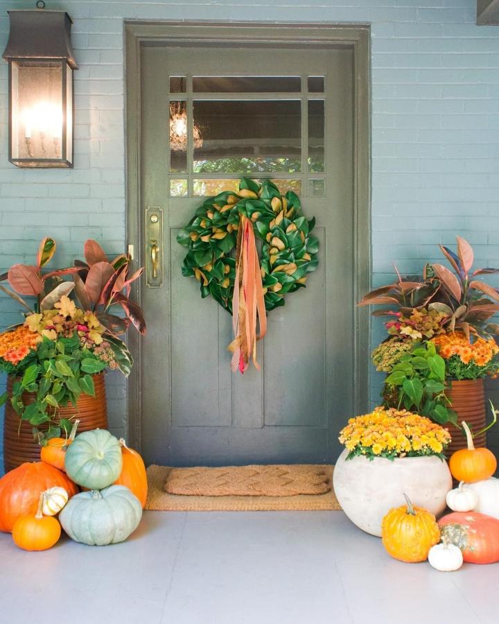 Colorful Fall Porch Planters from @cactusandtropicals. Pumpkins, mums, and a leafy wreath frame a dark door.