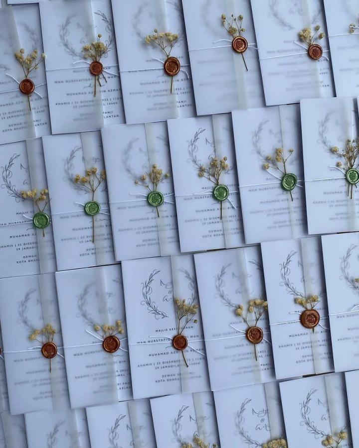 Soft gray vellum wedding invitations from @wishess.my. Rust wax seals, dried yellow flowers, and botanical sketches.