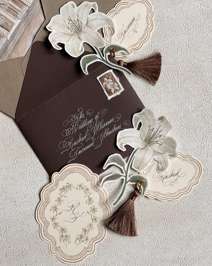 Cocoa brown floral invitation set from @syllablecalligraphy. Layered handmade wedding stationery with cream lilies and brown tassels.