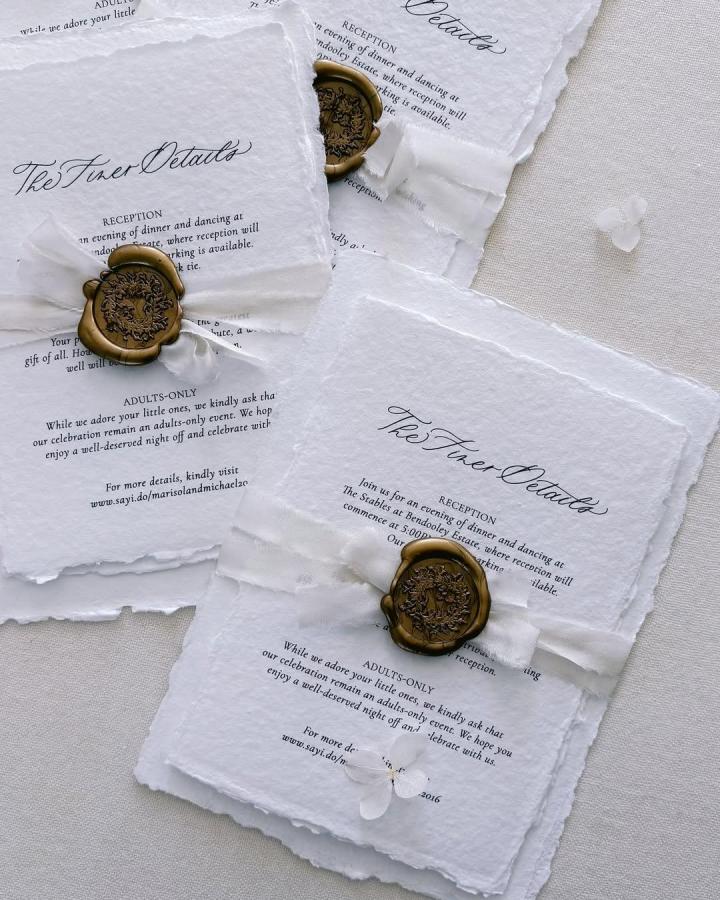White deckled paper invitation from @wishuponacalligraphy. Bronze wax seals and silk ribbon add handmade wedding stationery charm.