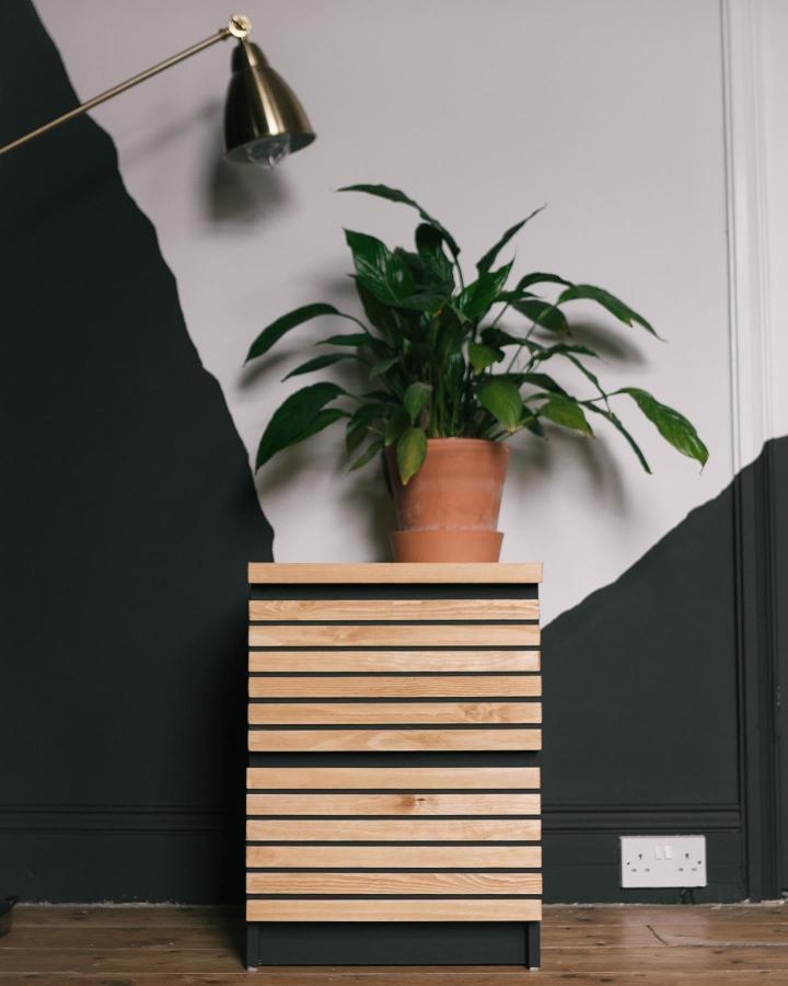Natural wood slat Malm dresser from @anotherfknflat. Black-painted frame with a leafy plant above.