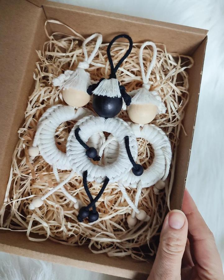 Ivory and black macrame animal ornaments from @plecione_. Wooden beads, loops, and tassels rest in a kraft box.