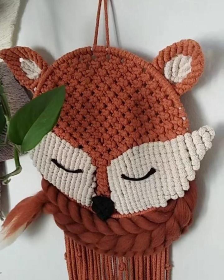 Terracotta and cream knotted macrame animal wall hanging from @mimobi_store. Fox face with fringe and leafy styling.