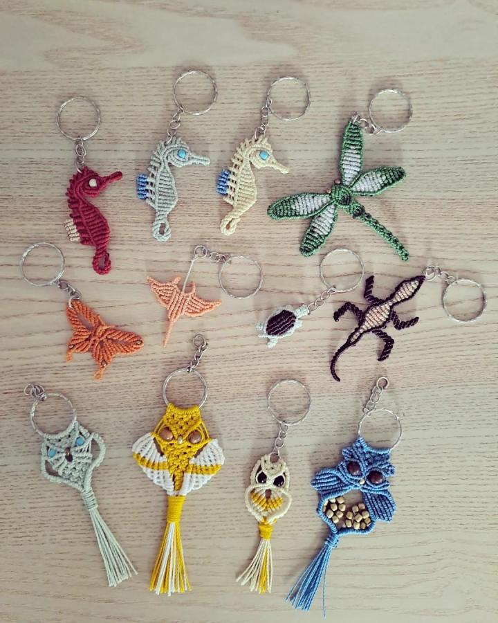 Colorful knotted animal keychains from @macrame.soul. Seahorses, dragonflies, butterflies, owls, and lizards rest on wood.