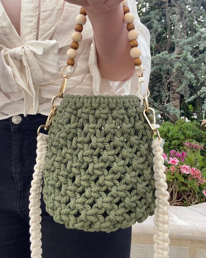 Olive green knotted macrame basket bag from @yarana.7. Cream braided straps and wooden bead handle add texture.