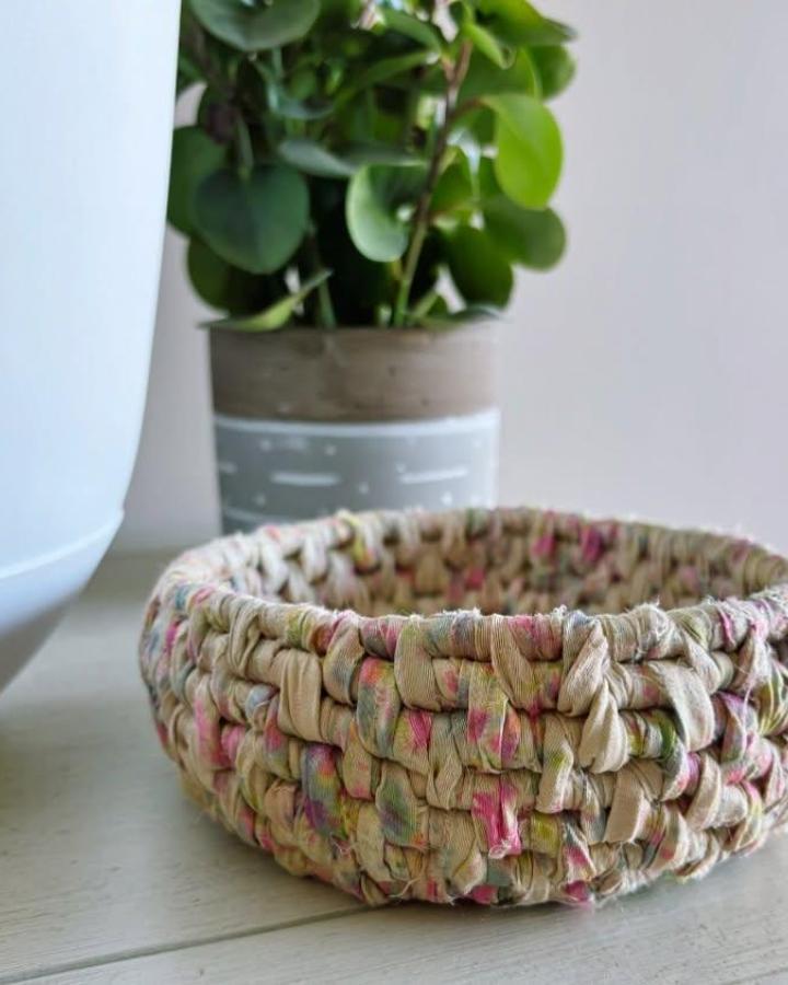 Cream floral braided plant basket from @knot_fornothing. Soft round holder beside a leafy houseplant.