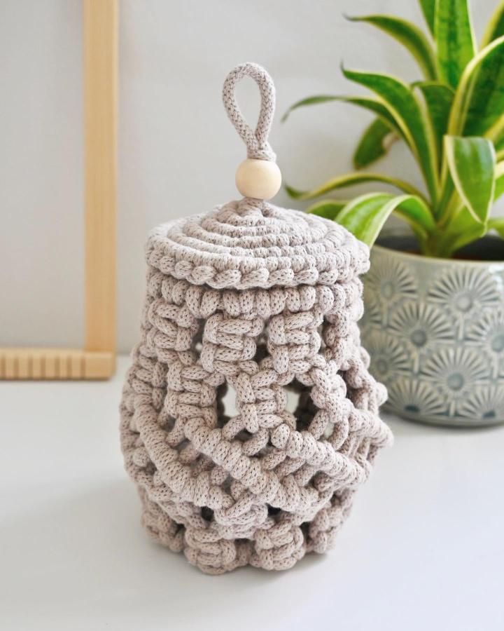 Light beige textured macrame basket from @_twome. Lidded craft design with wooden bead and loop handle.