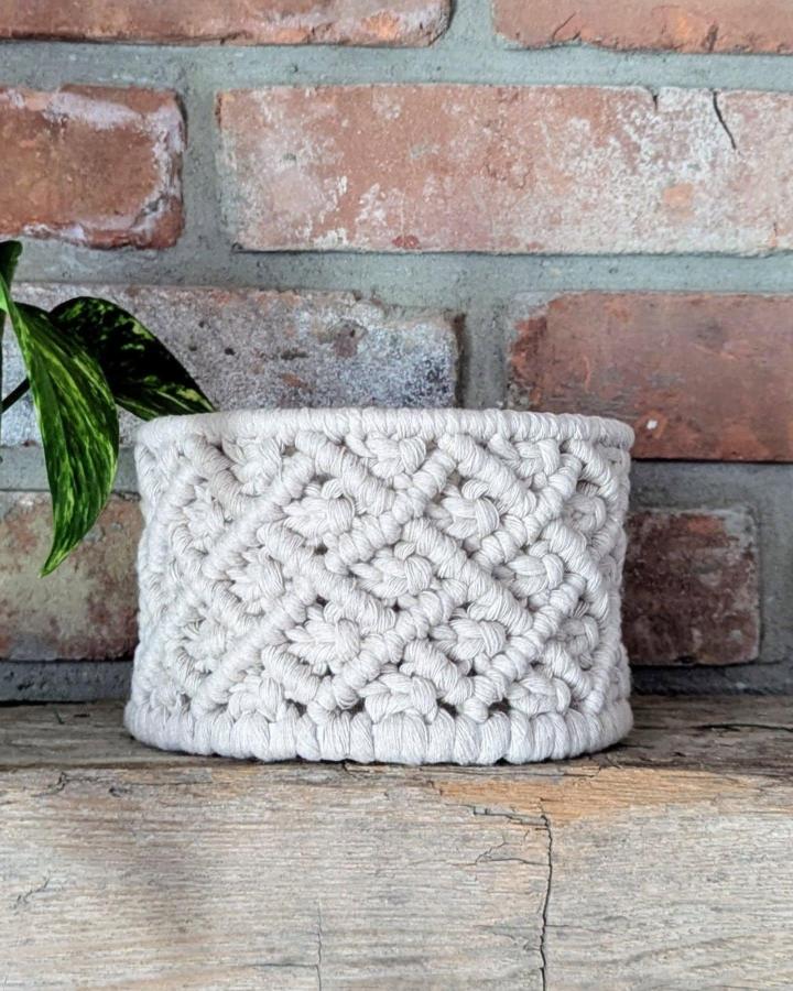 Ivory textured macrame basket ideas from @floralfeatherdesign. Knotted planter basket against brick.