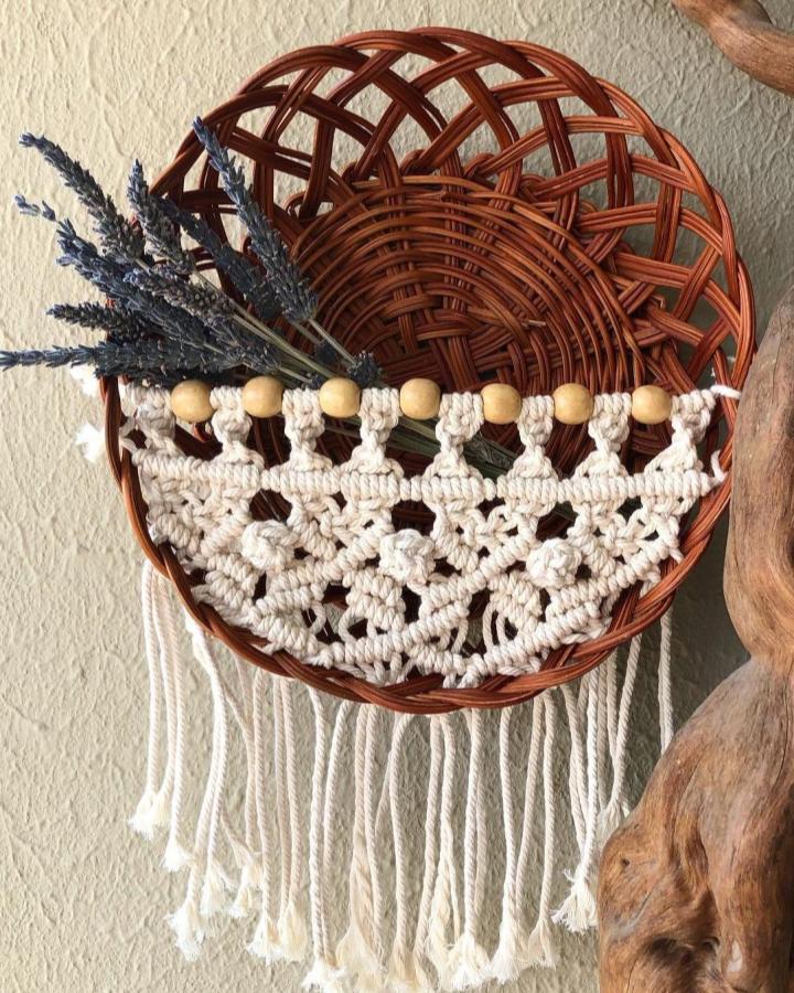 Cream macrame wall basket from @ensoshandmade. Woven rattan, wooden beads, lavender stems, and long fringe create a boho hanging.