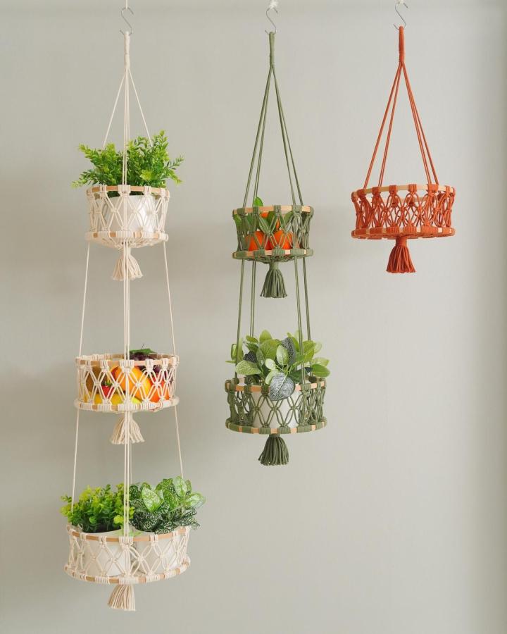 Ivory, olive green, and terracotta cotton cord hanging planters from @beandaikon. Tiered baskets hold leafy plants.