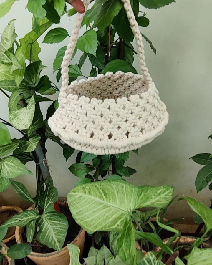 Cream textured hanging basket from @ethnichandicraft. Macrame basket ideas feature braided handles and a rounded woven body.