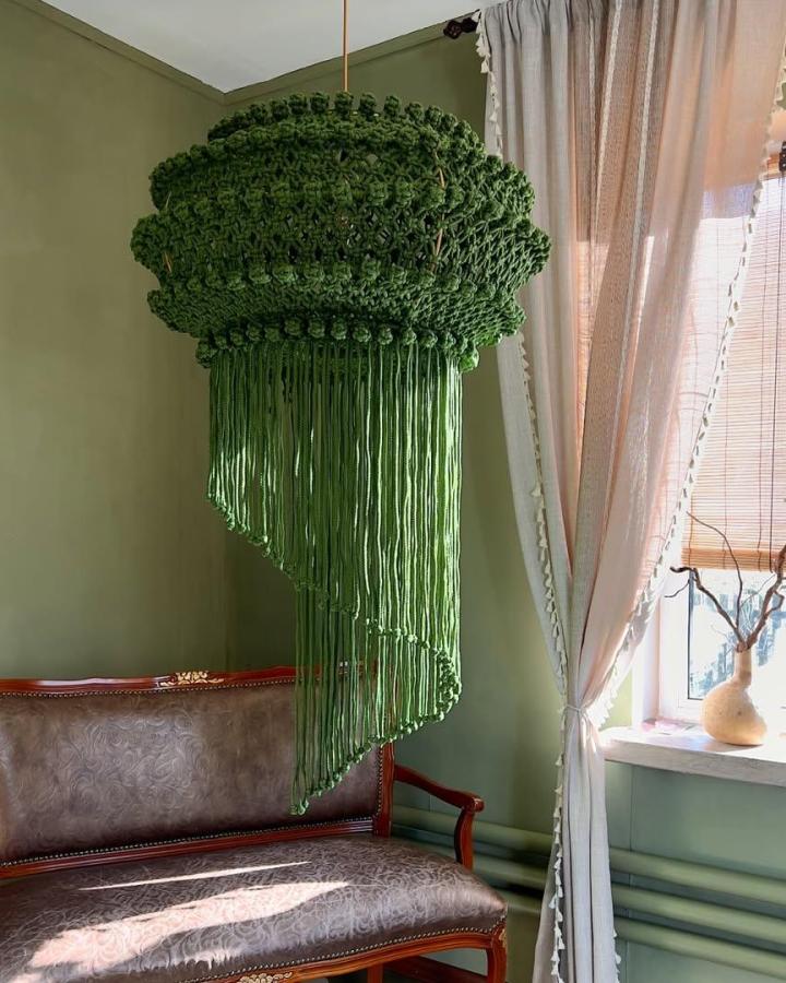 Deep green macrame chandelier from @macramespb. Layered knots and cascading fringe hang above a vintage settee.