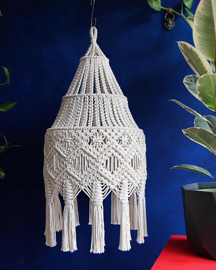 Ivory cotton macrame chandelier from @macramessage. Tiered knots and long fringe contrast with a deep blue wall.