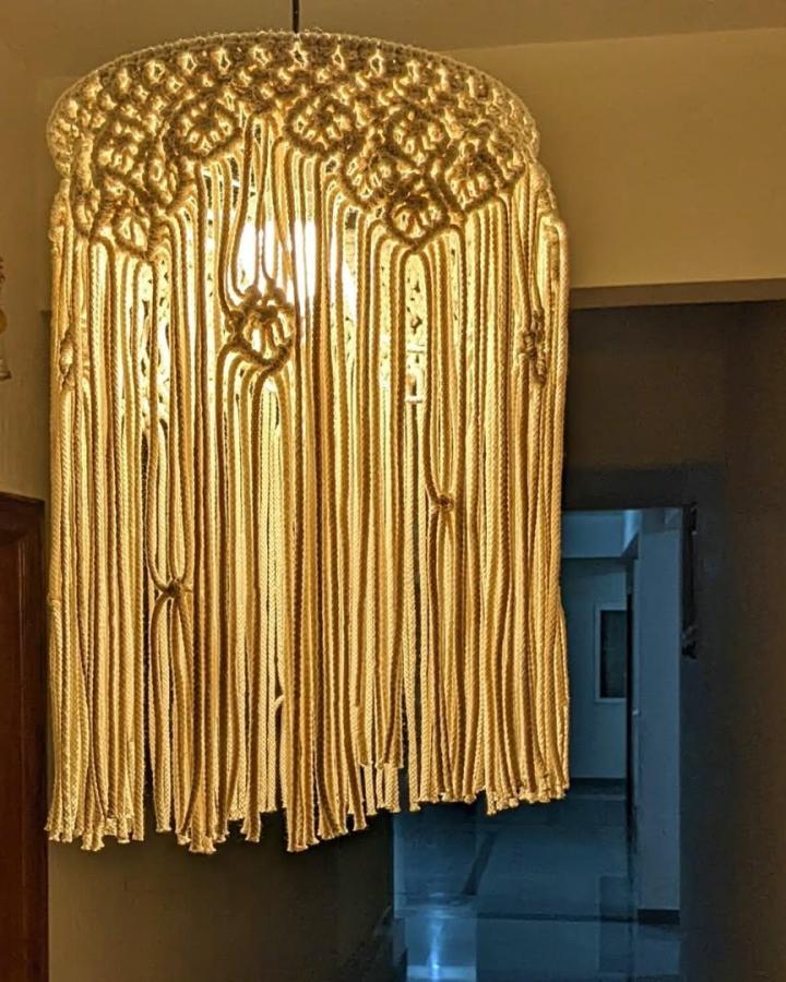 Cream woven macrame chandelier from @thetwistedjoy. Long fringe filters warm light above a dark doorway.