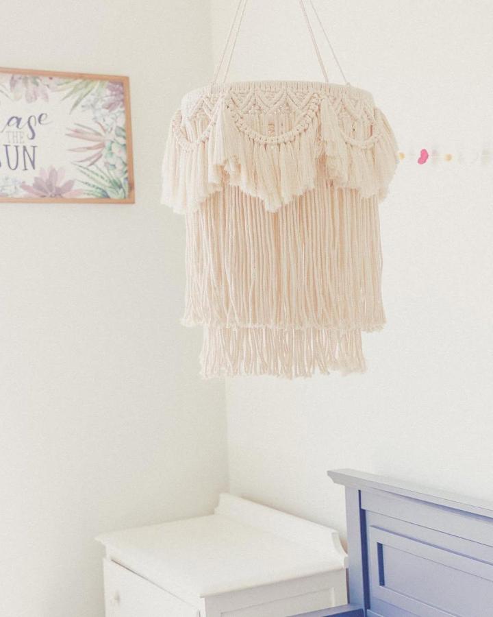 Cream layered macrame chandelier from @savbythesea__. Long cotton fringe hangs above a white bedroom dresser.